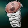 Silver and rose dial watch with moonphase display, secondary dial, and metal bracelet on green background.