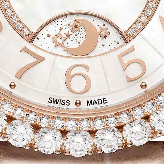 A close-up of the Jaeger-LeCoultre Rendez-Vous Night & Day watch face shows gold numerals, a moon phase with stars, "SWISS MADE" text, and a sparkling diamond-set pink gold border around this luxury women’s timepiece.