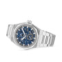 The Zenith Defy Skyline Skeleton is a luxury silver wristwatch with a blue skeleton dial, silver hour markers, and a metal link bracelet, shown at an angle for a bold urban look.