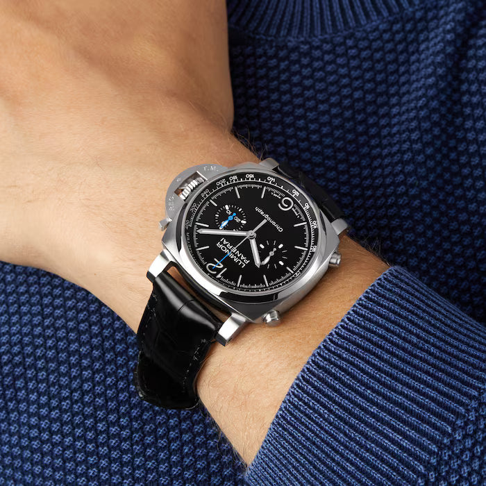 A person in a blue textured sweater wears a Panerai Luminor Chrono luxury sports watch with a black leather strap and detailed black dial on their left wrist.