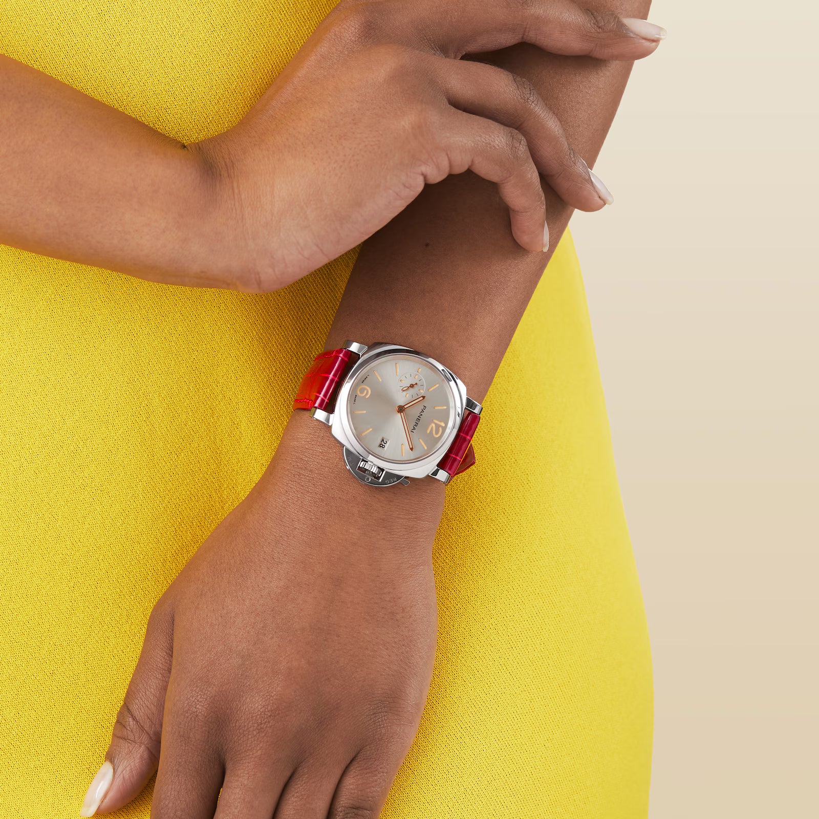 A person in a yellow dress wears a Panerai Luminor Due with a red strap on their left wrist, set against a simple light beige background that highlights the elegance of Italian design.