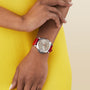 A person in a yellow dress wears a Panerai Luminor Due with a red strap on their left wrist, set against a simple light beige background that highlights the elegance of Italian design.