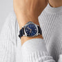 A person in a light gray ribbed sweater showcases a Panerai Luminor Due with a blue dial, silver case, and dark blue leather strap on their left wrist.