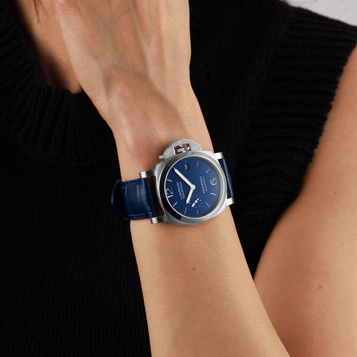 A person in a sleeveless black sweater showcases the Panerai Luminor Quaranta Automatic on their left wrist, featuring a blue dial and strap, stainless steel case, and an elegant small date window.