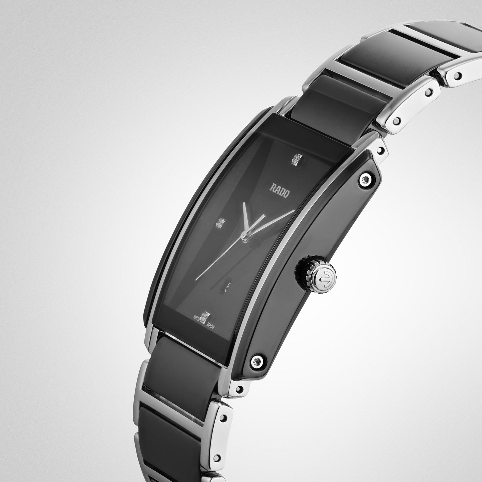 A close-up of the Rado Integral Diamonds watch, featuring a rectangular black and silver case, black dial with minimalist hour markers, high-tech ceramic, and a sleek metal bracelet.