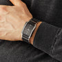 A person wearing a stylish Rado Integral Diamonds watch with a rectangular black and silver face and metal band, featuring quartz movement, rests their hand on a dark gray sweater.
