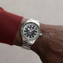 A persons wrist wearing a Rado Captain Cook Automatic watch with vintage details, featuring a green bezel and black dial, set against a neutral background.