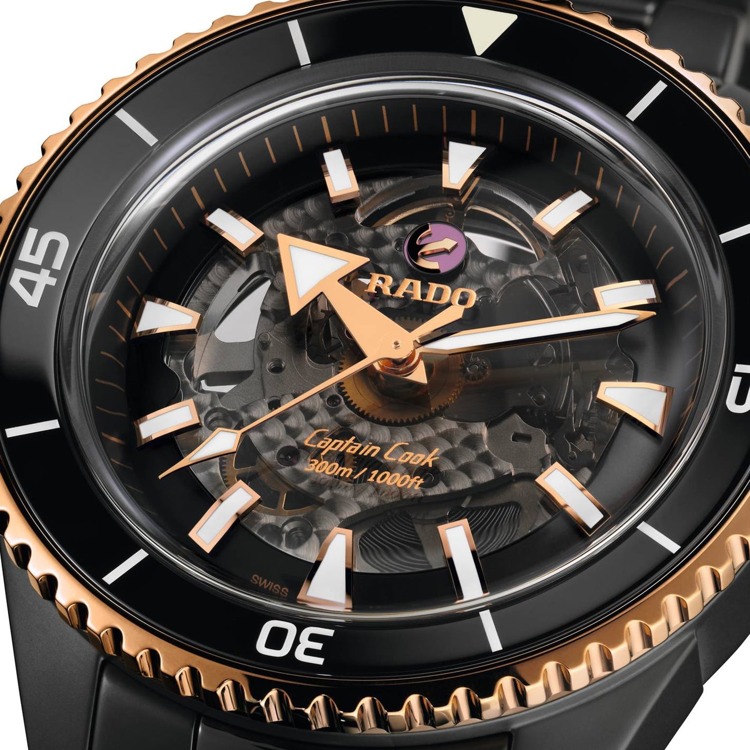 Close-up of the Rado Captain Cook High-Tech Ceramic wristwatch with a black and gold case, visible automatic movement, Nivachron™ hairspring, and 300m/1000ft water resistance shown on the dial.