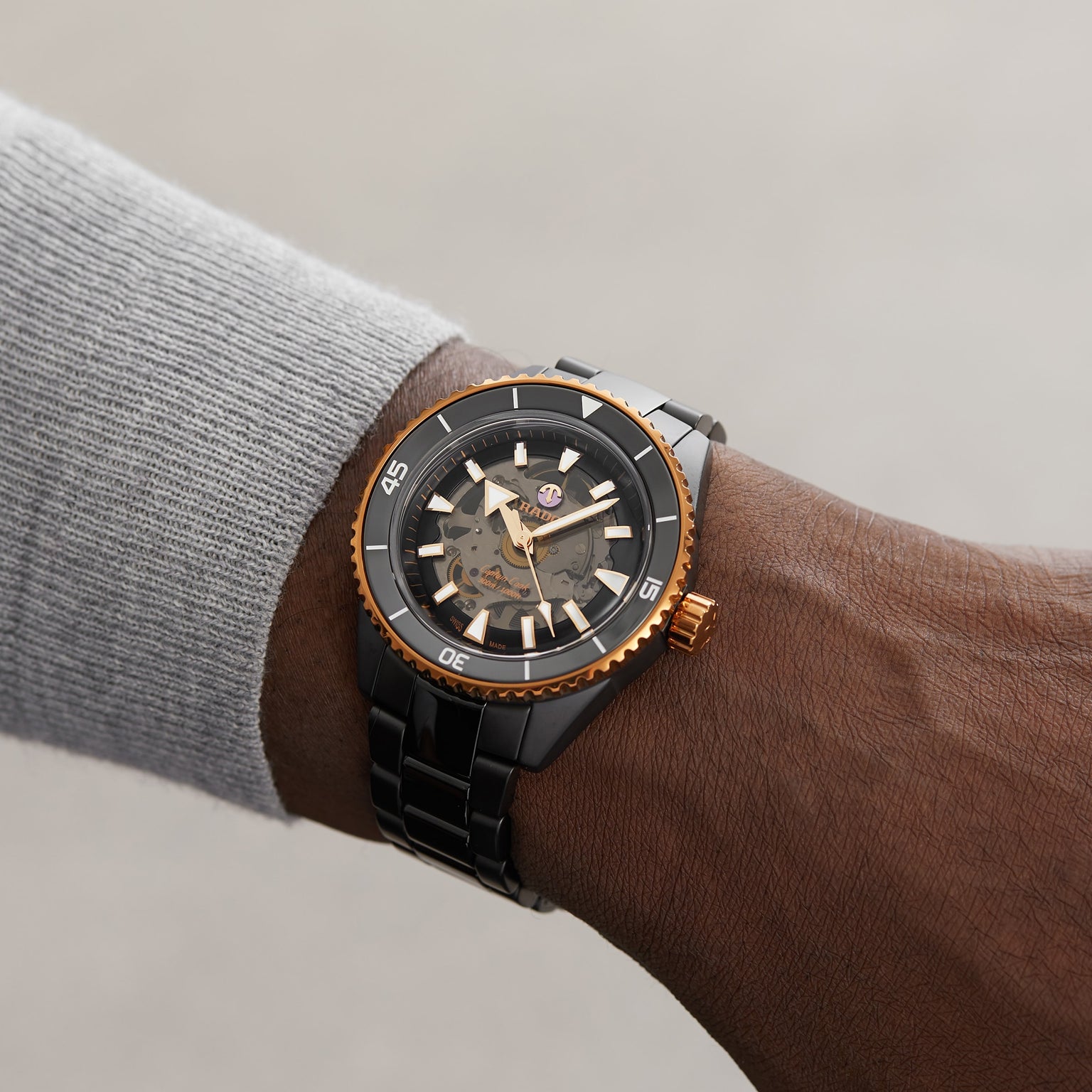 A person wearing a Rado Captain Cook High-Tech Ceramic wristwatch in black and gold, featuring a partially transparent dial that reveals the internal gears, set against a plain background.