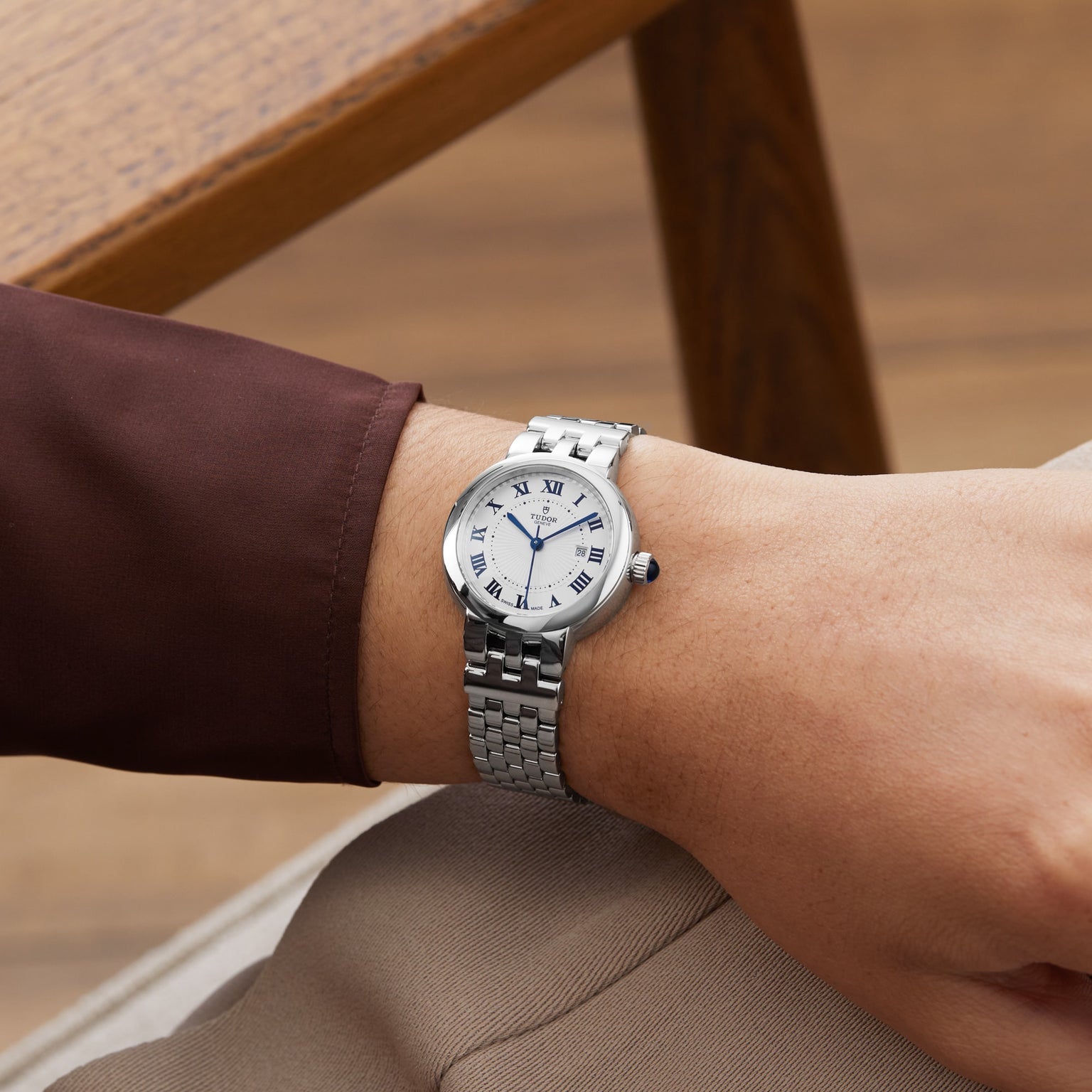 A TUDOR Clair de Rose silver wristwatch with a white face and Roman numerals worn on a persons wrist.