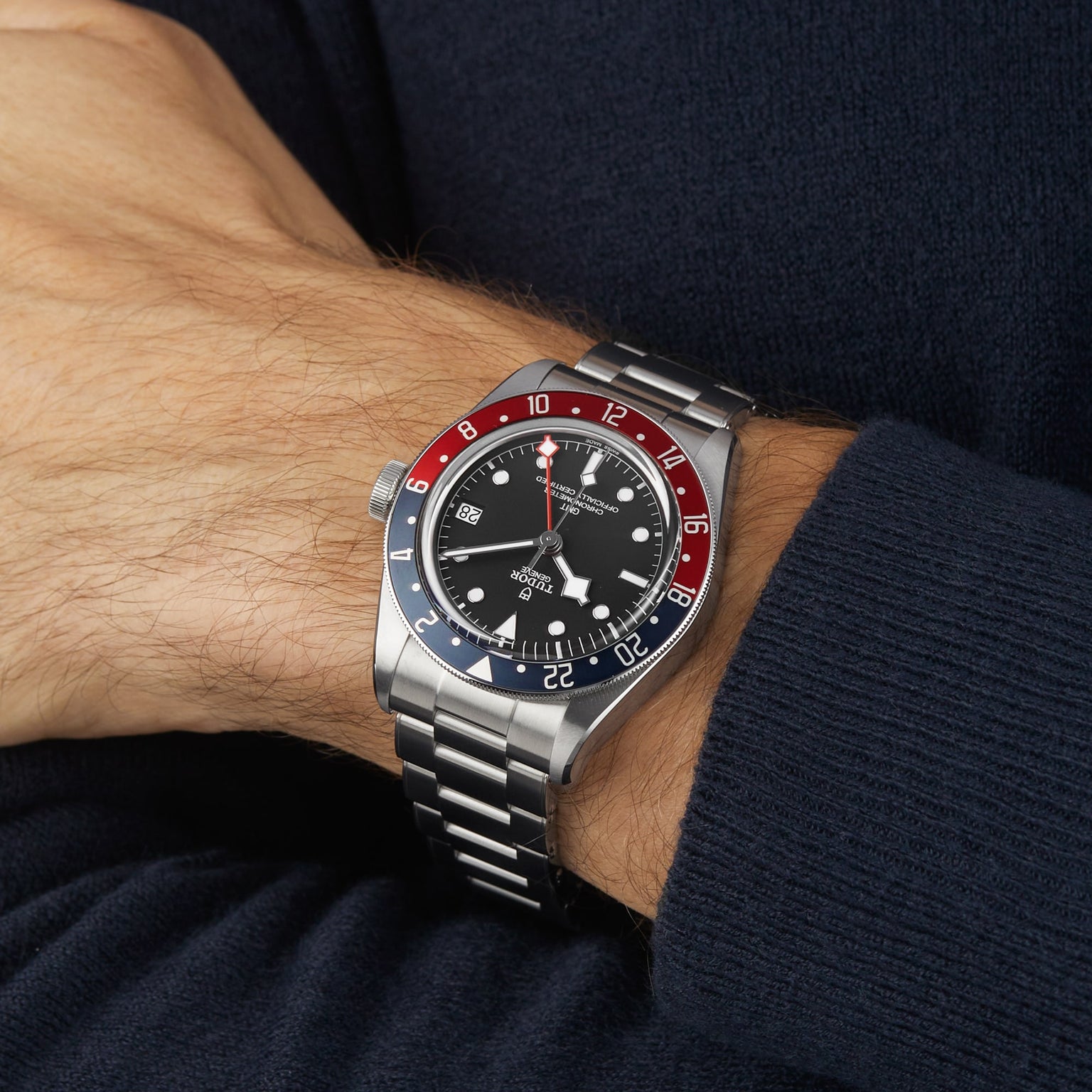 A TUDOR Black Bay GMT wristwatch with a black dial and red-blue bezel is worn on a person’s left wrist, paired with a dark long-sleeve shirt—a classic choice for diving watch enthusiasts.