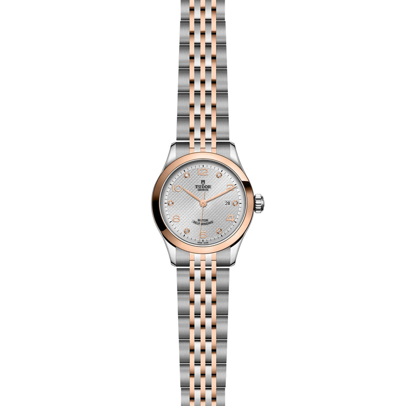 The TUDOR 1926 is a two-tone watch with a silver and rose gold bracelet, round silver dial, gold hour markers, rose gold bezel, date at 3 oclock, and powered by the mechanical caliber 2671.