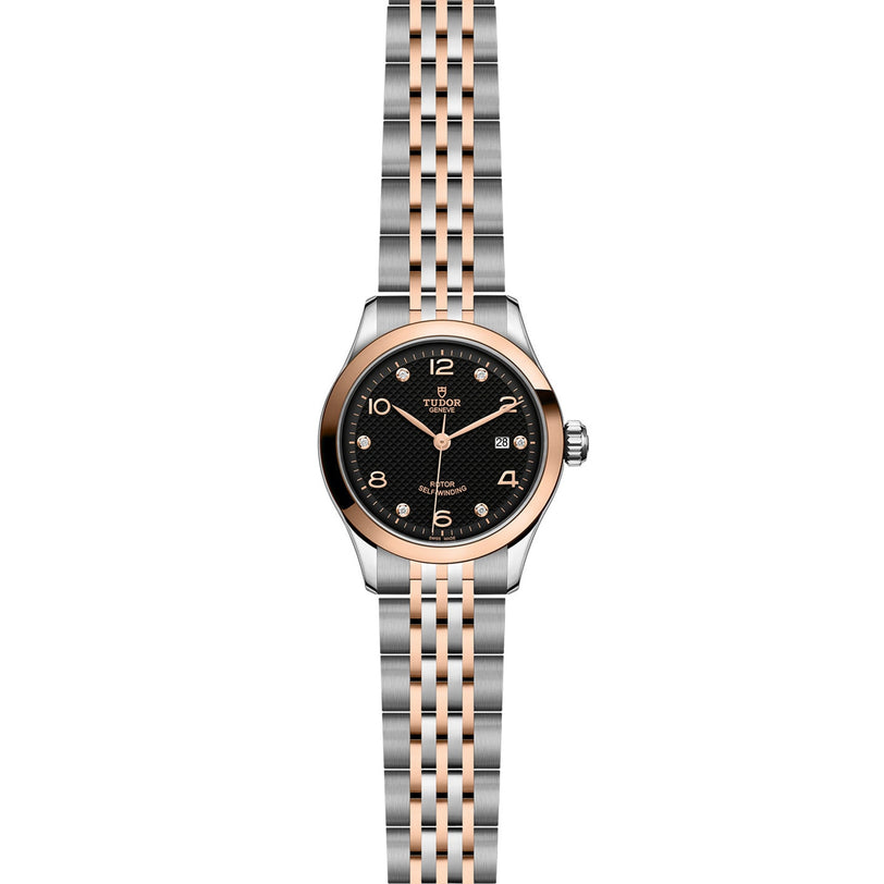 A TUDOR 1926 wristwatch with a black textured dial, gold Arabic numerals, date display, and a silver-and-gold metal bracelet is displayed against a white background.