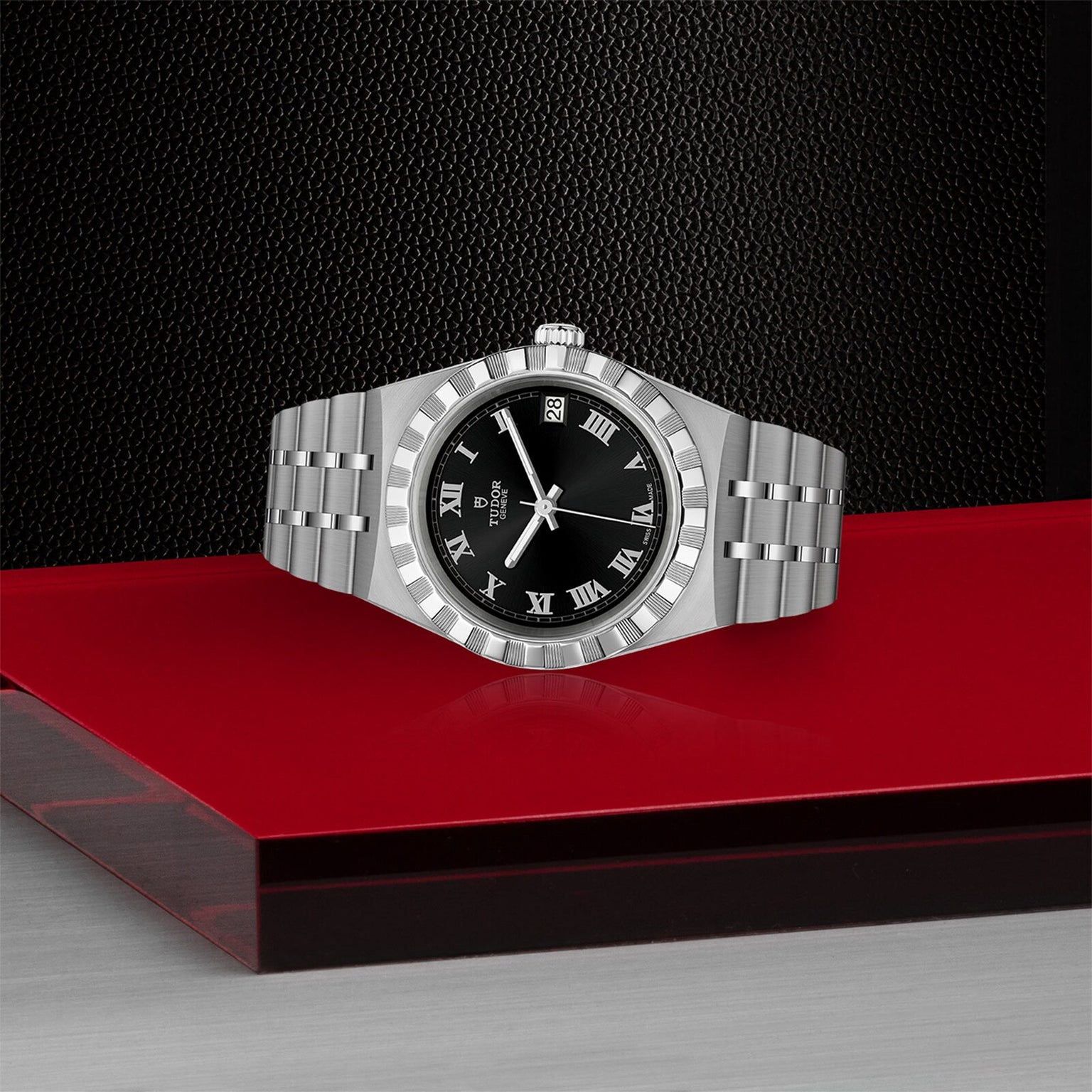 The TUDOR Royal wristwatch features a black dial, Roman numerals, and date window—an ideal choice for sport-chic enthusiasts. Shown on a striking red and black surface.