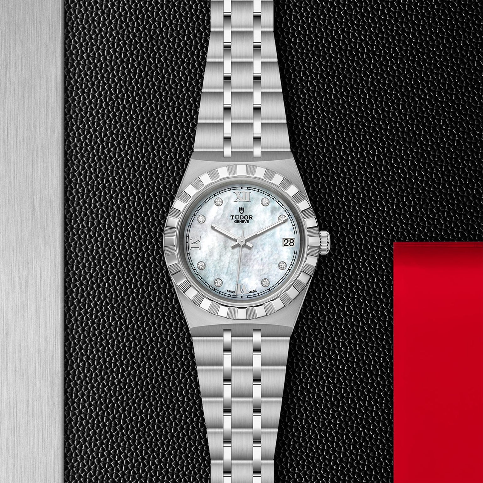 The TUDOR Royal, a stainless steel wristwatch with a mother-of-pearl dial, diamond hour markers, and date window—an automatic sport-chic timepiece—stands out on a textured black background with red and metallic highlights.