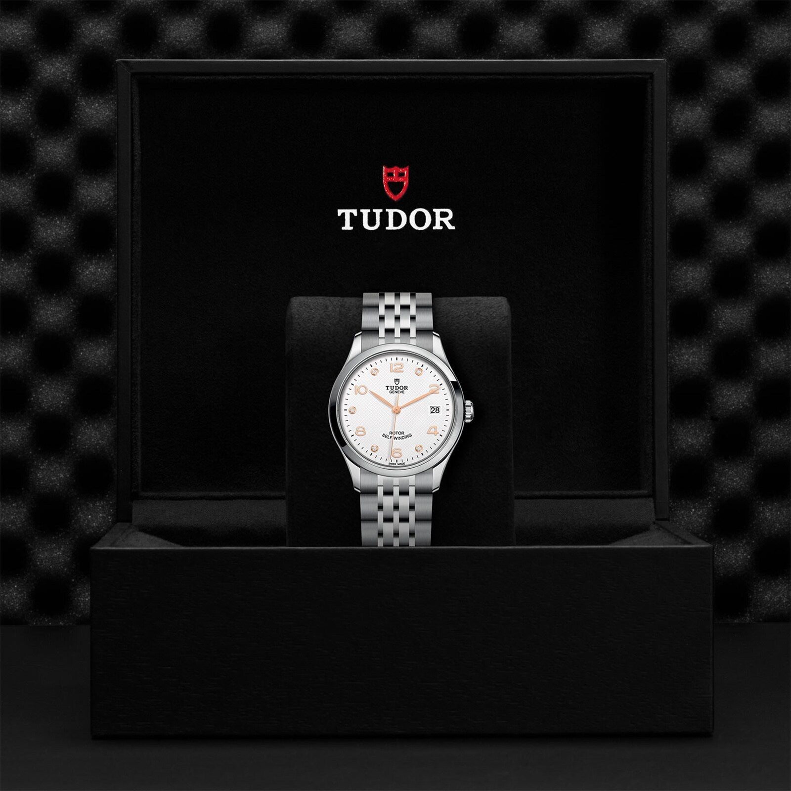 A TUDOR 1926 silver wristwatch with a white dial is displayed inside an open black TUDOR presentation box.