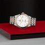 A TUDOR 1926 two-tone wristwatch with a white dial, gold hour markers, and a metal bracelet is showcased on a red and black platform.