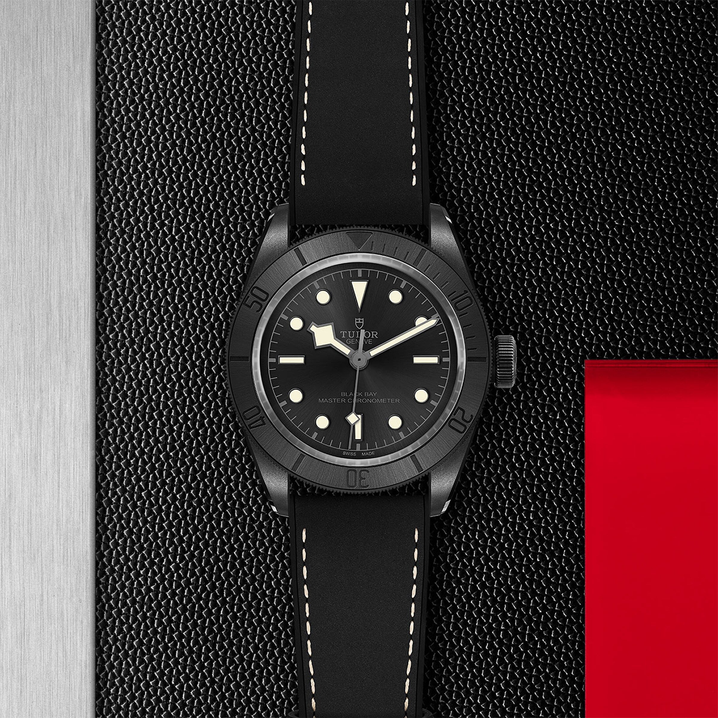 TUDOR Black Bay Ceramic wristwatch with a black strap, displayed on a textured black and red background.