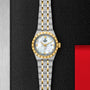 The TUDOR Royal, a two-tone gold and silver watch with a mother-of-pearl dial, is displayed on a textured black surface.