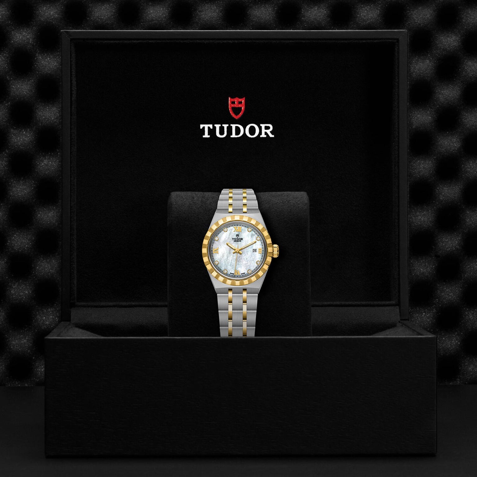 A TUDOR Royal wristwatch with a gold and silver band displayed in a black TUDOR box.