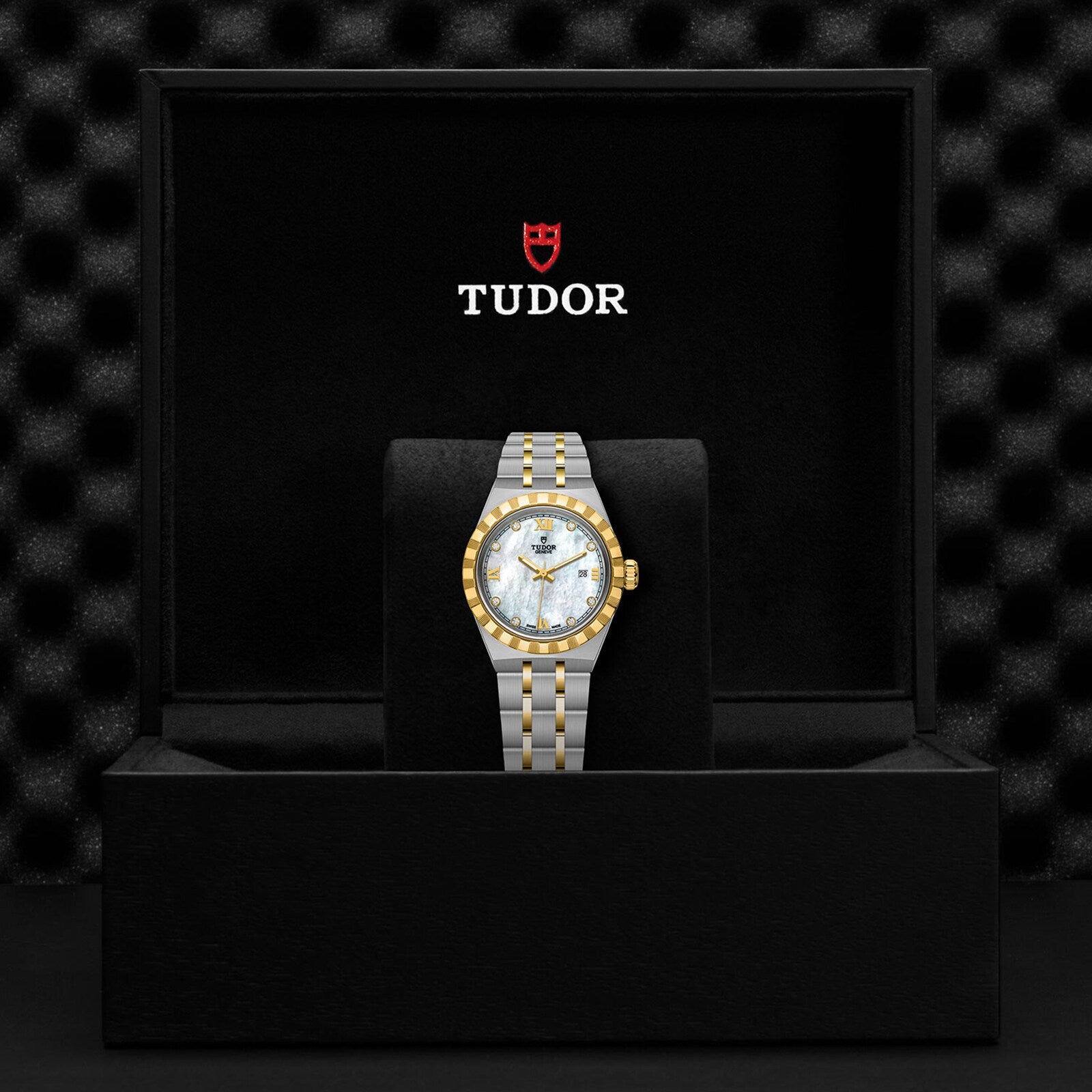 A TUDOR Royal wristwatch with a gold and silver band displayed in a black TUDOR box.