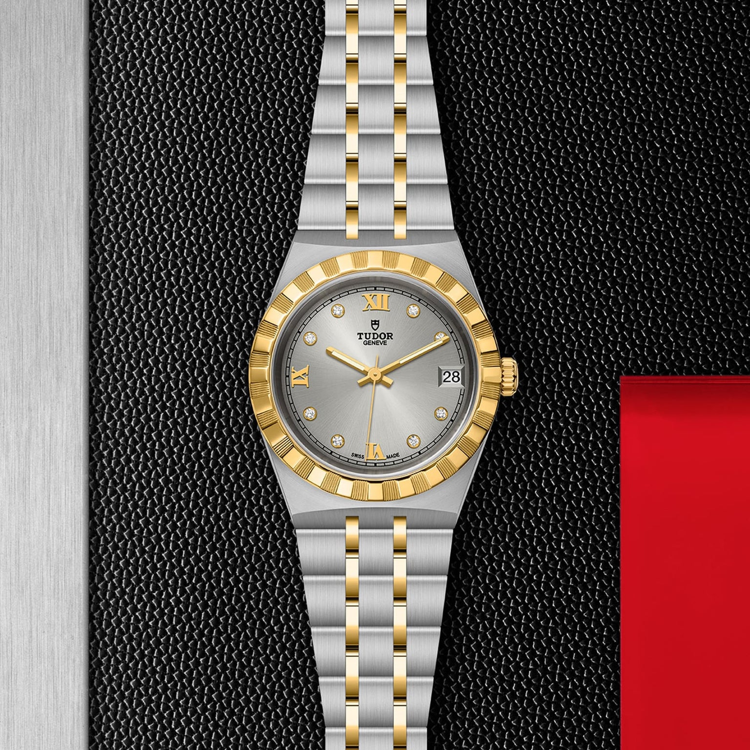 A TUDOR Royal wristwatch with a silver dial, gold hour markers, fluted bezel, and two-tone bracelet rests on a textured black surface.
