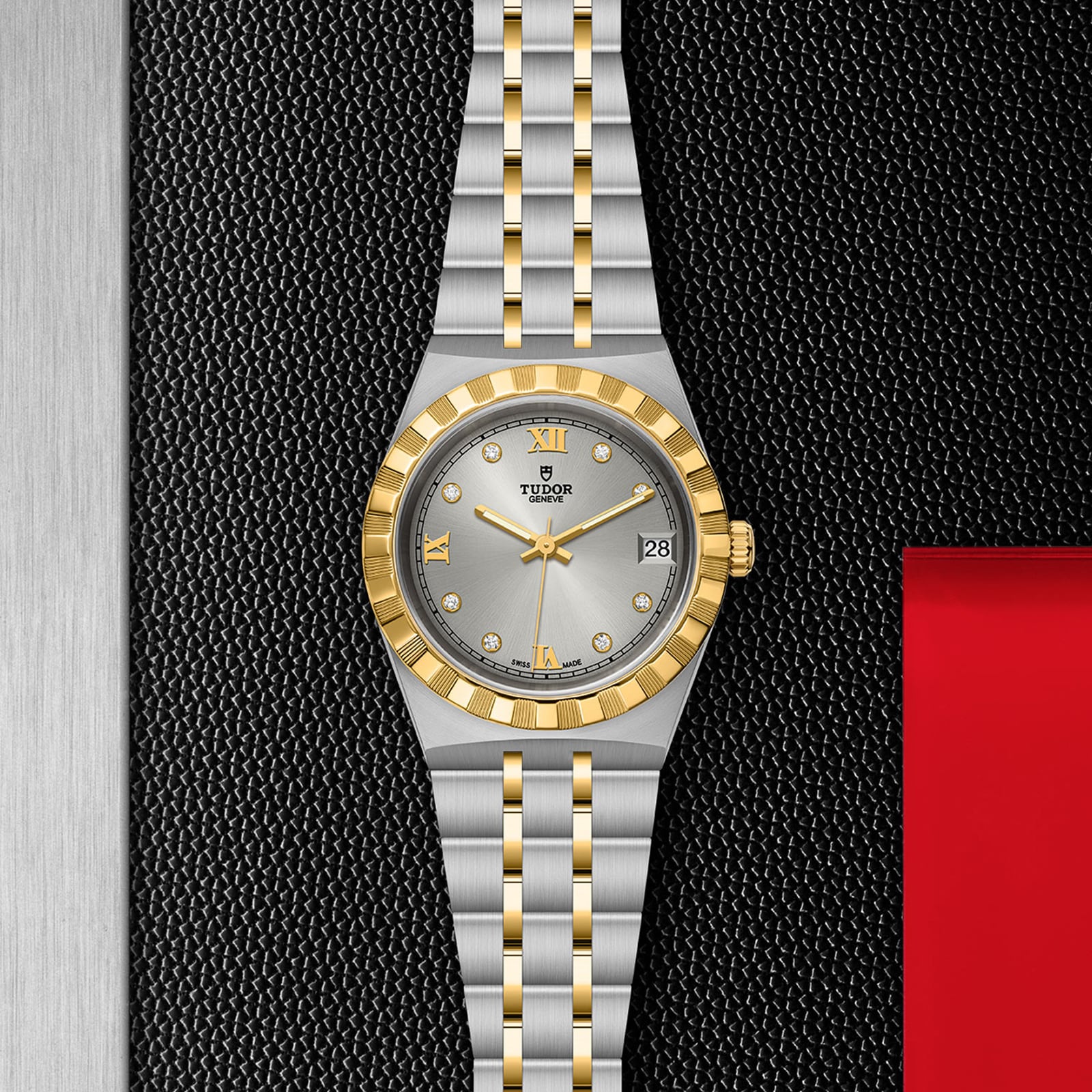 A TUDOR Royal wristwatch with a silver dial, gold hour markers, fluted bezel, and two-tone bracelet rests on a textured black surface.