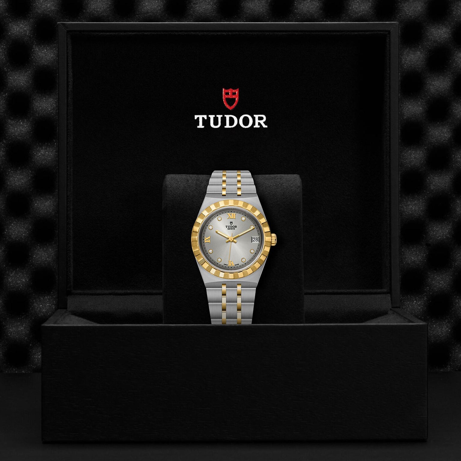 A TUDOR Royal automatic watch with a stainless steel and gold bracelet is showcased in an open black box, displaying the TUDOR logo on the inside lid.