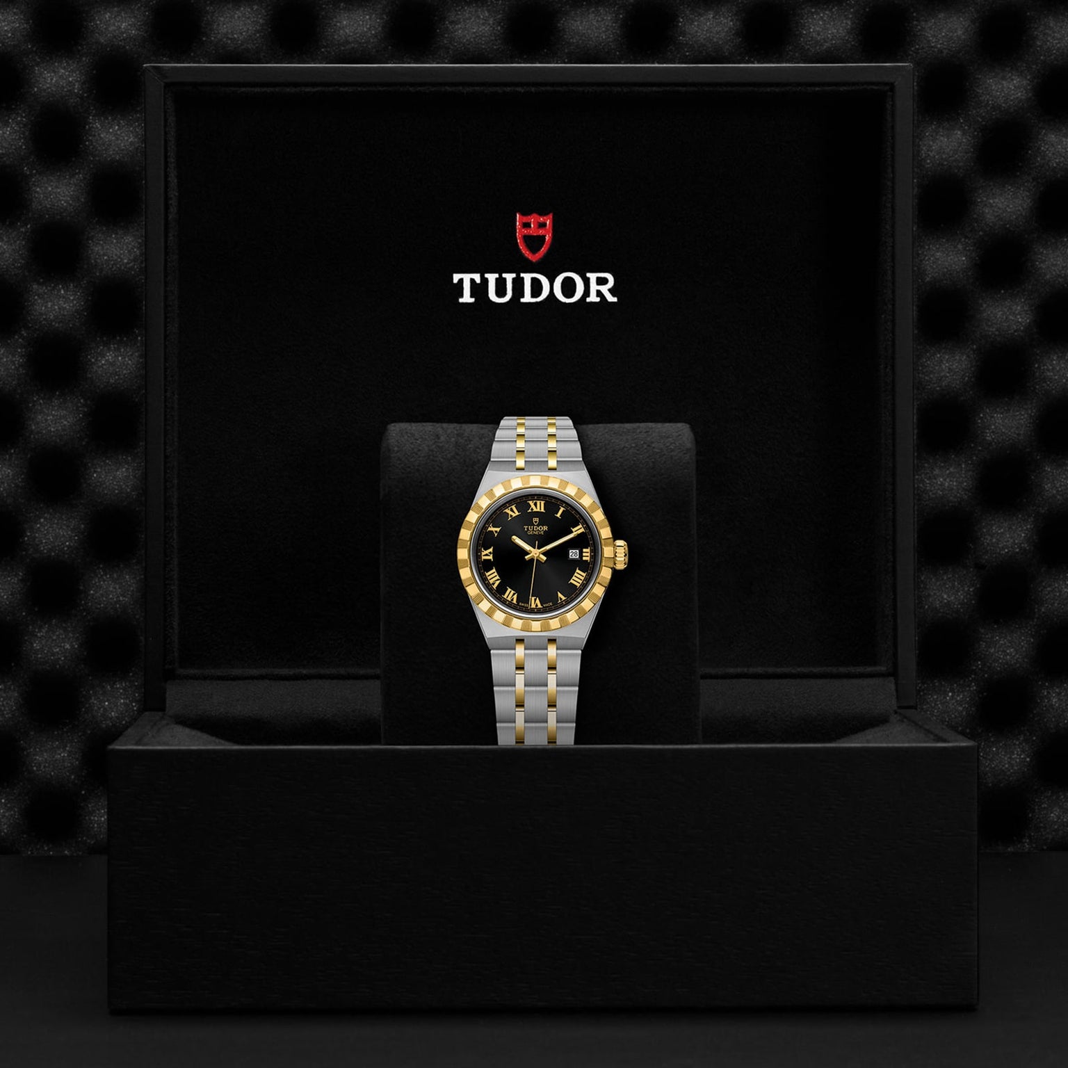 A TUDOR Royal wristwatch, featuring a stainless steel and gold two-tone band with a black-and-gold bezel, is presented in an open Tudor-branded black box, exemplifying the refined sport-chic style of automatic watches.
