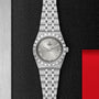 The TUDOR Royal blends stainless steel and gold with Roman numeral markers and a date display, set on a textured black and metallic background with red accents—a striking automatic sport-chic wristwatch.