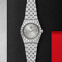 The TUDOR Royal, a silver wristwatch with metal bracelet, fluted bezel, diamond markers, and date display, is shown on a black and red textured background—a refined automatic sport-chic timepiece.