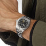 A person wearing a TUDOR Black Bay Pro—stainless steel with a black dial and 24-hour bezel—dressed in a dark green jacket, reflecting the heritage of Tudor divers’ watches and modern watchmaking.