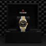 A TUDOR Black Bay One 41 S&G wristwatch with a black and gold face and two-tone metal band is displayed upright in an open black TUDOR box.