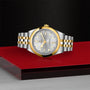 A two-tone silver and gold TUDOR Black Bay One 41 S&G watch rests on a red and metallic surface with a textured black background.