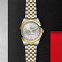 A TUDOR Black Bay One 41 S&G wristwatch, featuring a silver and gold finish with a white dial, displayed on a textured black and silver background.