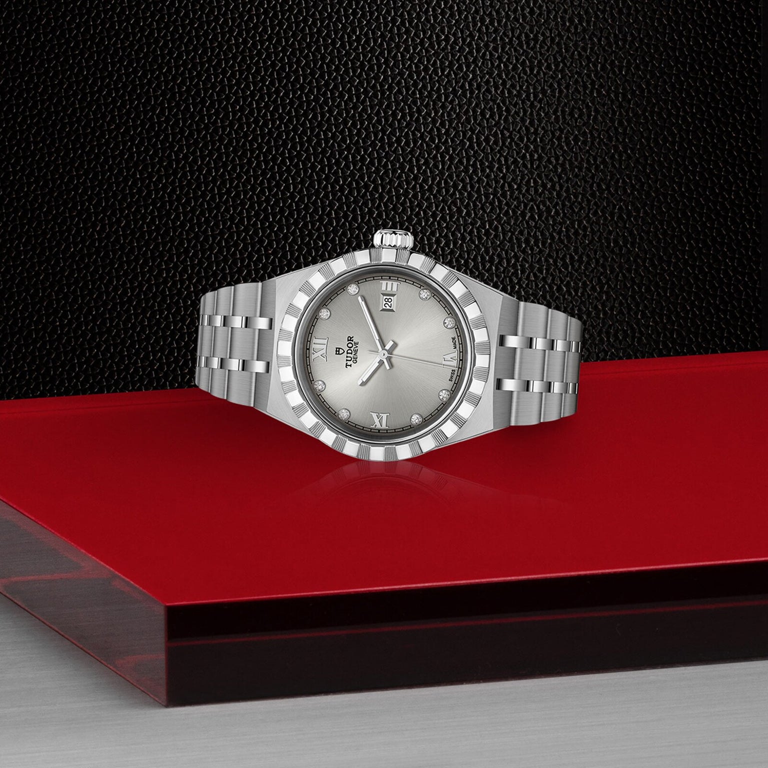 A TUDOR Royal silver wristwatch with a metal bracelet is displayed on a red and black textured surface.