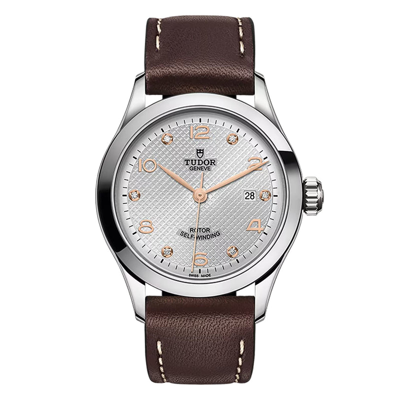 A silver TUDOR 1926 wristwatch with a textured dial, gold numerals, date display, and brown leather strap is shown on a white background.