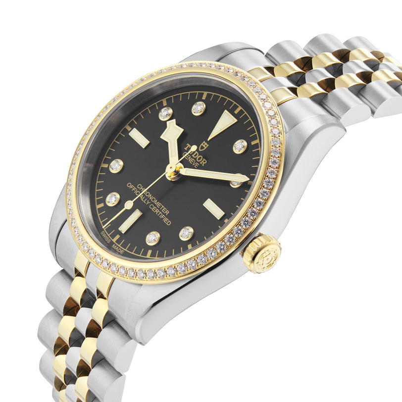 The TUDOR Black Bay One 36 S&G wristwatch features a black dial, diamond-set bezel, yellow gold accents, and a stainless steel and gold bracelet, displayed against a white background.