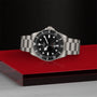 The TUDOR Pelagos 39 is a stainless steel professional dive watch with a black dial and bezel, displayed on a red and black surface against a textured dark background.