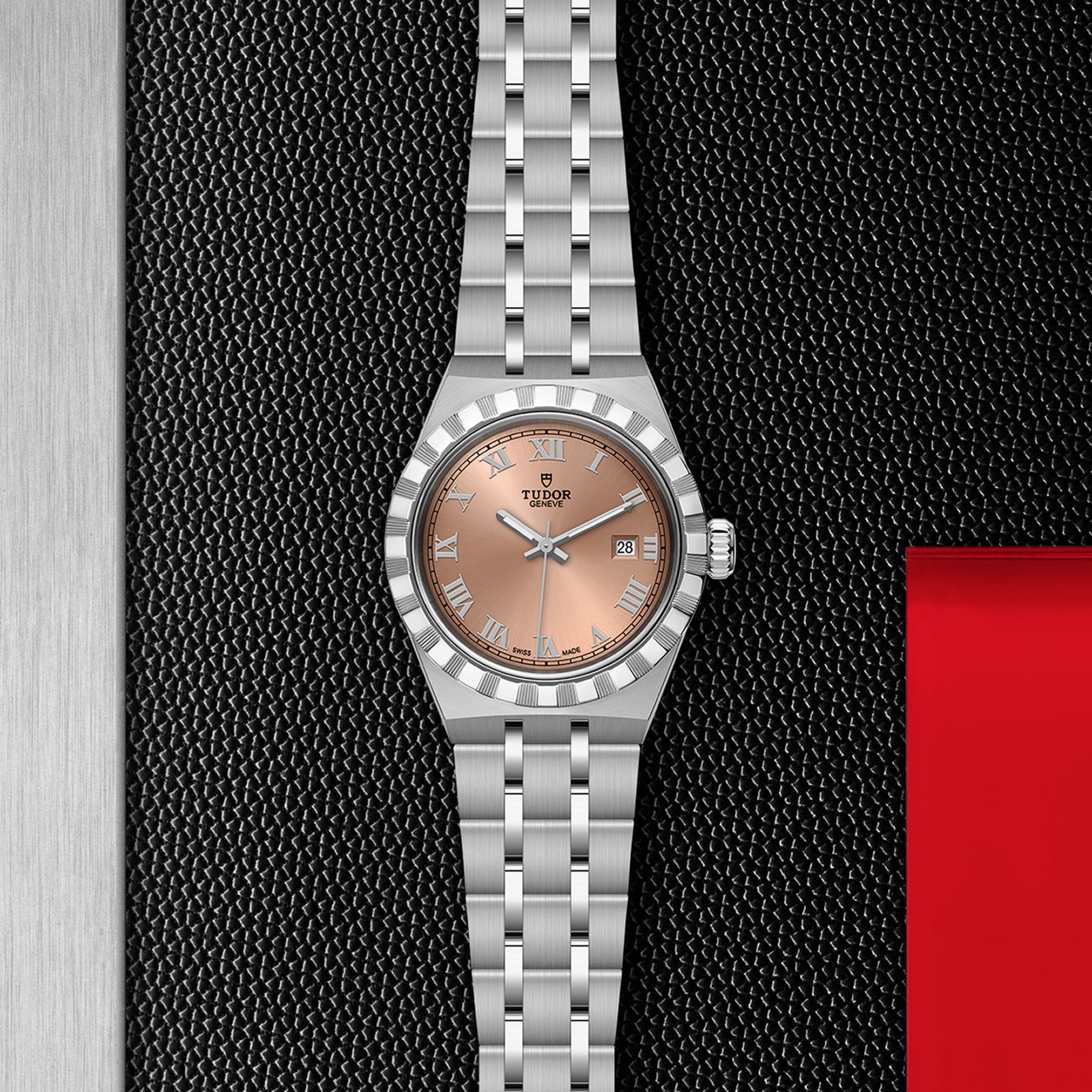 A TUDOR Royal wristwatch with a stainless steel case, salmon-colored dial, and Roman numerals is displayed on a textured black and red background, highlighting its refined automatic movement.