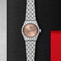 A TUDOR Royal wristwatch with a stainless steel case, salmon-colored dial, and Roman numerals is displayed on a textured black and red background, highlighting its refined automatic movement.