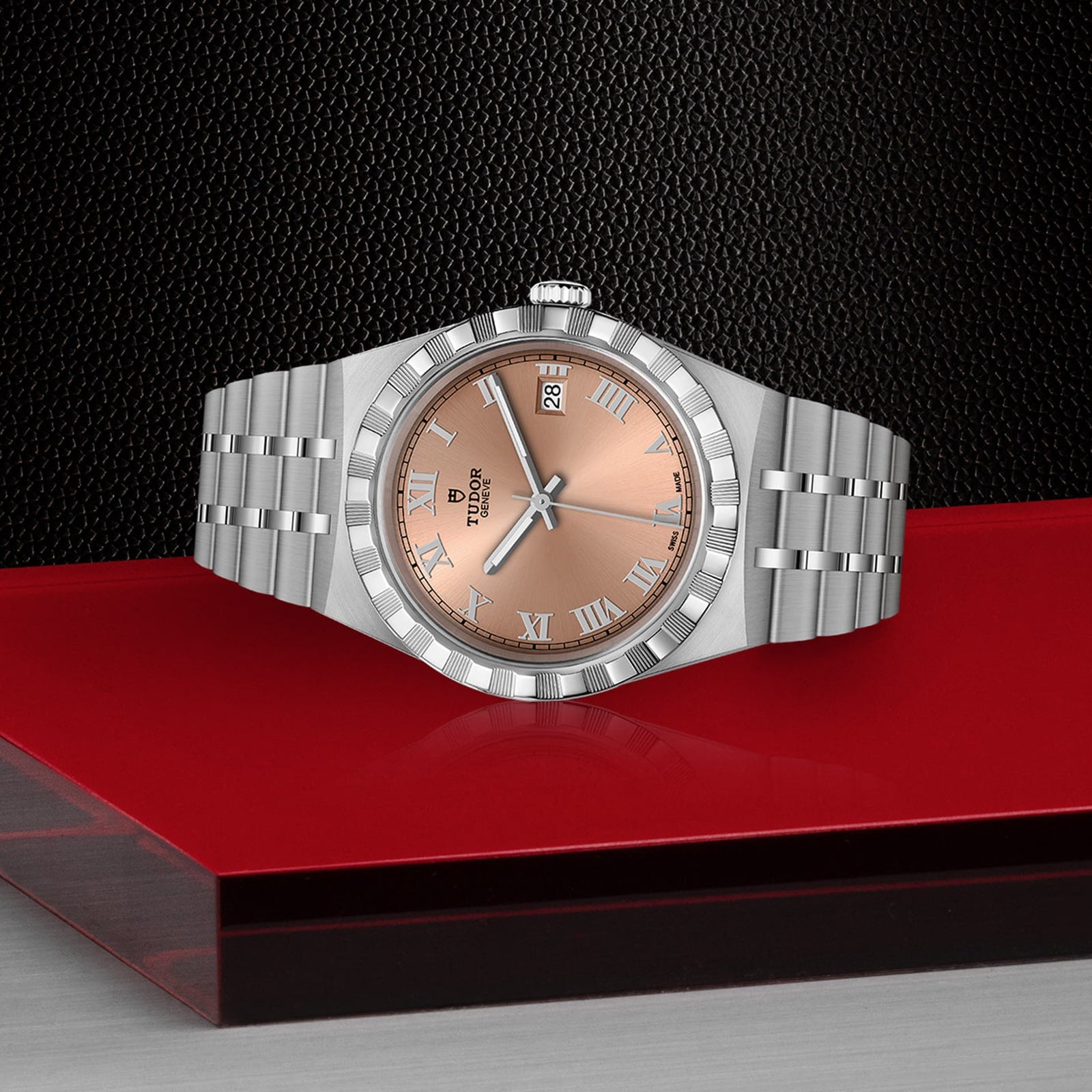 A TUDOR Royal wristwatch with a silver case and salmon dial lies on a red and black geometric surface.