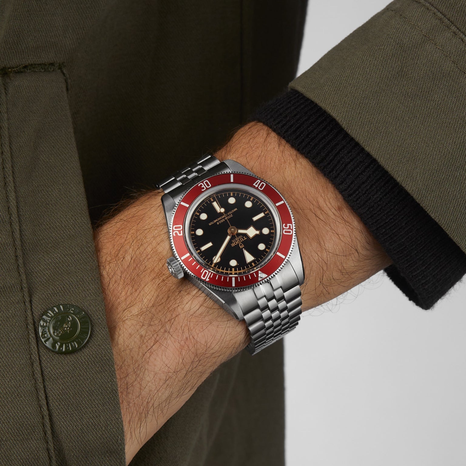A person in an olive green jacket wears a TUDOR Black Bay watch with a burgundy bezel and black dial.