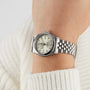 A TUDOR Black Bay One 31 wristwatch with a metal band on a persons wrist, paired with a white knit sweater.
