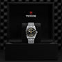 A TUDOR Black Bay One 36 unisex watch with a black dial and 316L steel bracelet is displayed in an open black TUDOR box, the logo clearly visible inside the lid.