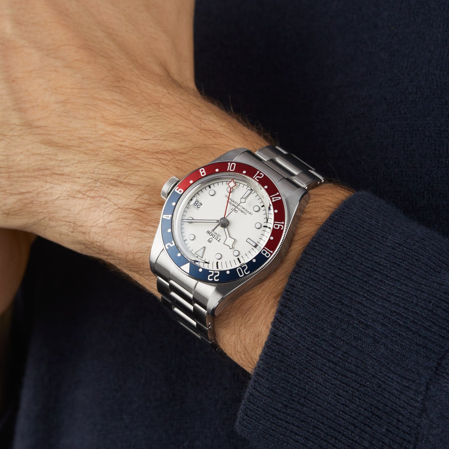 A TUDOR Black Bay GMT wristwatch with an opaline dial and red-blue bezel is worn on a person’s left wrist, visible against a dark long-sleeve shirt.