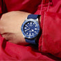 A person wearing the TUDOR Pelagos FXD, a blue diver’s watch with a navy strap, and a red jacket covered in water droplets.