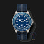 The TUDOR Pelagos FXD features a blue dial and bezel, a blue fabric strap with grey stripe, and a Marine Nationale emblem—making it a distinctive modern diver’s watch.