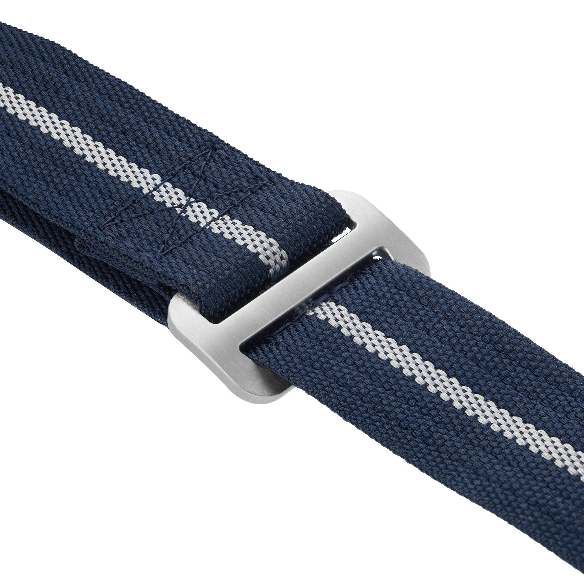 Close-up of a navy blue fabric strap with a gray metal buckle and a central white stripe, inspired by straps on the TUDOR Pelagos FXD watch.
