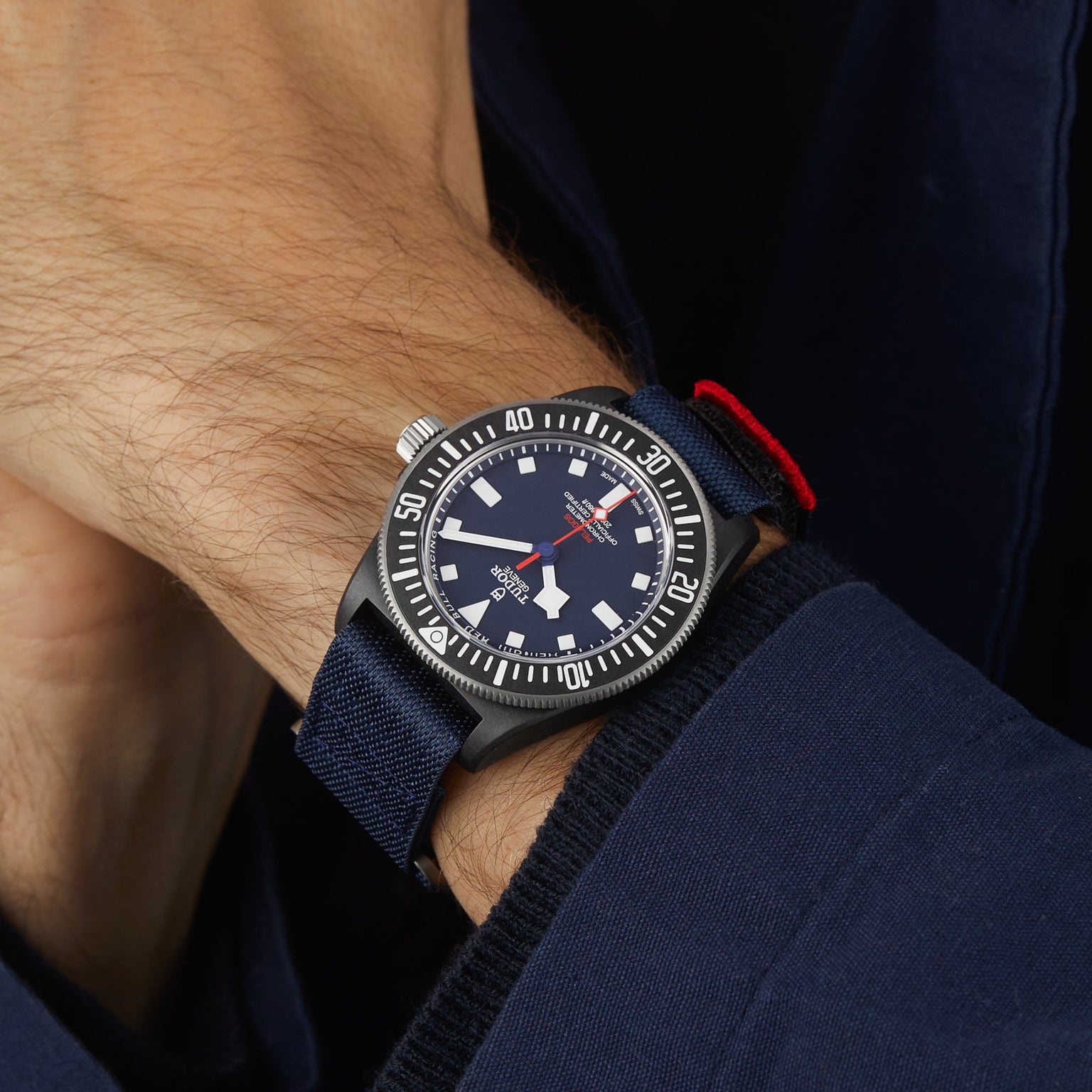 A person wearing a TUDOR Pelagos FXD diver-style watch with a navy blue case, black bezel, white markers, and a waterproof navy blue fabric strap.